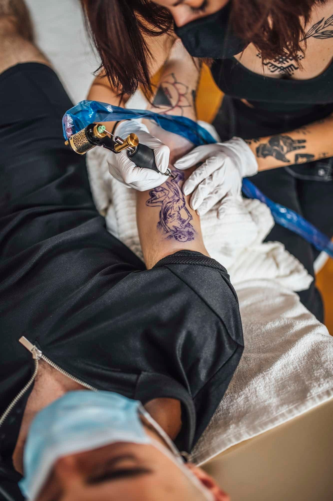 Top View of Female Tattoo Master Tattooing Man’s Arm in a Studio